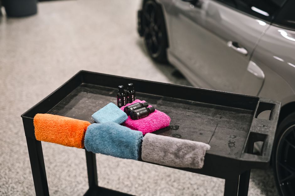 Colorful towels and detailing products on a cart beside a car in a garage.